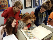 Students and professor looking at book, as described in caption. 