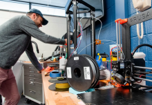 Student staff member performing maintenance on 3d printers on a workshop table.