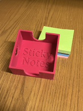 Pink 3d printed sticky note holder sitting on tabletop with stack of colorful stick notpads