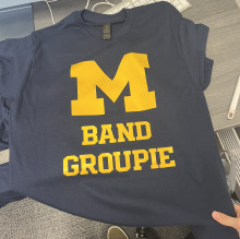 A blue t-shirt with yellow text that says Band Groupie with a Michigan M