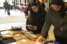 Students perusing a table full of books wrapped in paper bag material.