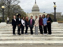A diverse group of women engineers from the University of Michigan are standing in front of the Capitol Building in Washington, D.C. wearing formal business attire