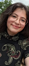 A woman with wavy, shoulder length-hair, brown-wire glasses, and a black shirt with swirling patterns, smiles at the reader