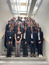 A diverse group of students in business casual stand on stairs for a photo