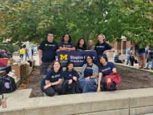 Members of the Student Library Engagement Ambassador Team (9 individuals) stand and sit around the Shapiro Library sign