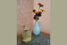 A greenish beverage garnished with mint, sits on a table next to a vase of flowers
