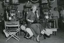 woman sitting on a man's back on a set with cameras and director's chair 