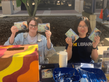 Library Student Ambassadors Roe Halbert and Grace Tai smiling and holding squirrel postcards.