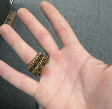 A hand showing off a wooden ring on the ring finger. The hand is white, palm facing up, and the ring has a V design to articulate the wood.