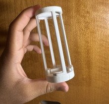 A hand holding a white 3D printed holder. It is a cylindrical container with four small supports. 