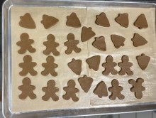 Cookie sheet with dark brown cut-out cookies in the shape of trees and gingerbread men on it