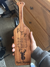 A wooden paddle with the greek letters Beta Gamma Chi, the bible quote 1 Corinthians 13.11, a buck head, and the name "Wyatt Wojdula" in cursive at the bottom.