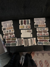 A top-down image of a collection of 10 white 3d printed organizer trays with small indented sections to separate parts. most of the trays are filled with various game pieces and small tokens.