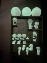 3D printed 3-story shelves built to look like a house with stairs and platforms. The smiski figurines are positioned on it across the layers, and the room is dark, showing the figurines glowing in the dark.