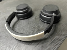 A pair of black over-the-ear headphones with a white 3D printed support band attached to the headband. 