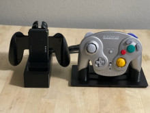 Two black 3D printed stands - one is holding Nintendo switch controllers, and a controller case, and the other is holding a nintendo Gamecube controller. All controllers are being held "standing up".