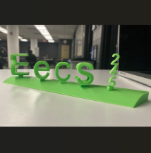 3D printed lime green letters stand on a white table. The nameplate shows two different words when looking at it from different sides - here, it says "EECS 245".