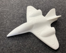 A small white 3d printed model of a fighter jet on a dark gray background