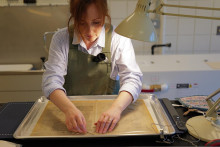 conservator in lab with hands extended over pages from a rare book in a treatment bath