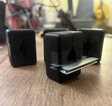 Four black 3D printed brain matrices standing vertically on a wooden table. Each matrix is a rectangle, and on the long side (the "top") has a divot with several small stripes for blades to slide through to cut the brain into slices.