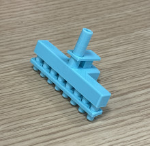 A blue 3D printed 8-channel aspirator adapter on a wooden table. The print is vertical, with one tube going into the base and eight tubes coming out of the bottom.