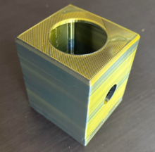 gold and green iridescent square shaped button and trackball holder on a grey grained wood background.