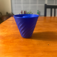 Blue coffee filter attachment on a honey grain wooden table with partial view of a chair and venetian blinds in the background.
