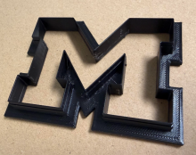 black 3d printed block M logo cookie cutter on manila background