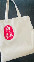A white cloth bag with a red vinyl printed logo on a bluish grey background