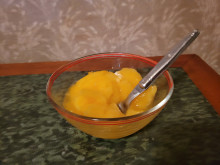 A mound of orange sorbet in a clear glass bowl on a green table