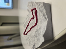 A gray, layered 3D model sits on a table, featuring a prominent red line that traces a bike trail along a section of the Andean mountain range, highlighting the trail’s path over varied elevations.