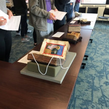 manuscripts displayed on a long table with students examining them and taking notes with pencil and paper