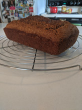 A brown rectangular loaf of bread cools on a wire rack on a white kitchen counter.