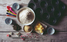 Image of an assortment of baking utensils, a bowl of flour, sugar, and butter as well, arranged on a woodent table