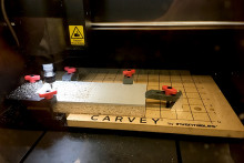 A tabletop carving machine cuts through a piece of linoleum.