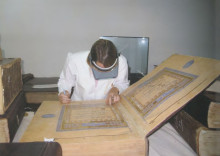 conservator in white coat examines massive manuscript volume