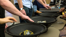 Several students place their hands on loudspeakers filled with percussion instruments.