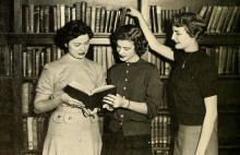 Three women reading a book together in a library setting