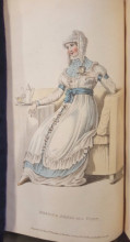 Woman in a blue and white dress siting on a pale yellow sofa, drinking tea